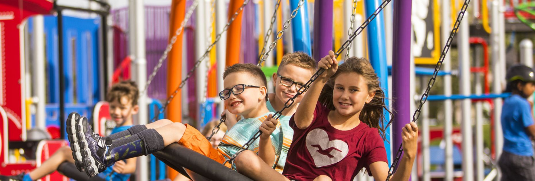 kids swing on a large, round multi-user swing at a colourful school playground