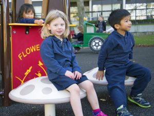 two children dressed in navy blue perch on Blue Imp toadstool seats at a playground in Toronto, Ontario