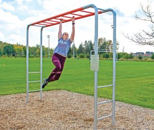 young woman in athletic clothing makes her way hand over hand across an orange-and-silver Blue Imp Horizontal Ladder designed for outdoor fitness use